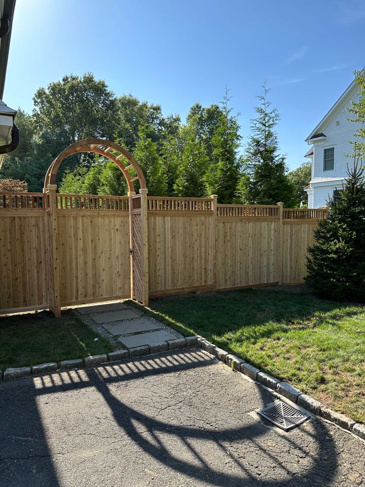 A stunning new cedar cap and trim fence in Westport with several beautiful custom details - a capped picket top and a 5 foot arbor with diagonal lattice side panels - which only enrich the classic cedar look. The unseen details matter too - our crew installed matching cedar boards along the bottom of the fence, burying portions into the ground to protect our customer’s dogs, keeping them safely inside.